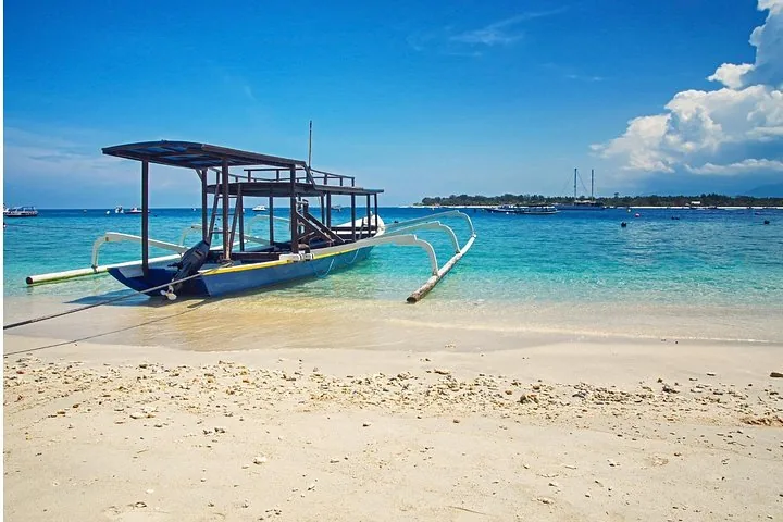 Barco tradicional de balancín amarrado en una playa de arena blanca con aguas azules cristalinas.