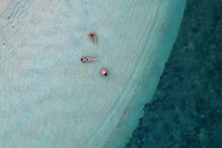 Toma aérea de tres personas nadando en aguas turquesa poco profundas y cristalinas.