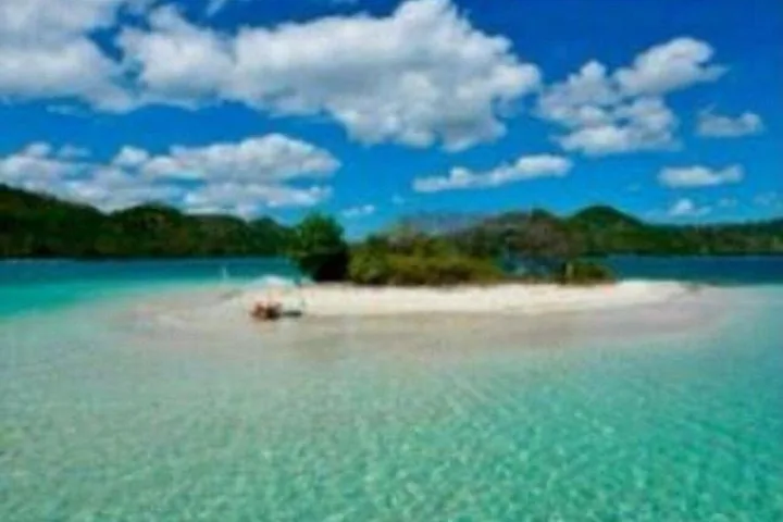 Kleine Insel, umgeben von flachem türkisfarbenem Wasser und Bergen in der Ferne.
